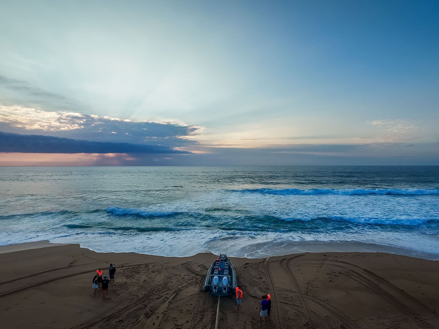 Aerial view of a boat with twin outboards resting on the sand at the water's edge beneath a dramatic sky