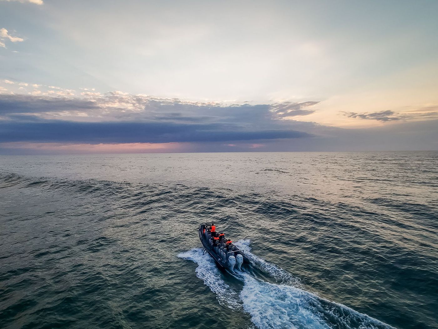 Aerial view of a boat with twin outboards heading out to sea beneath a pastel dawn sky