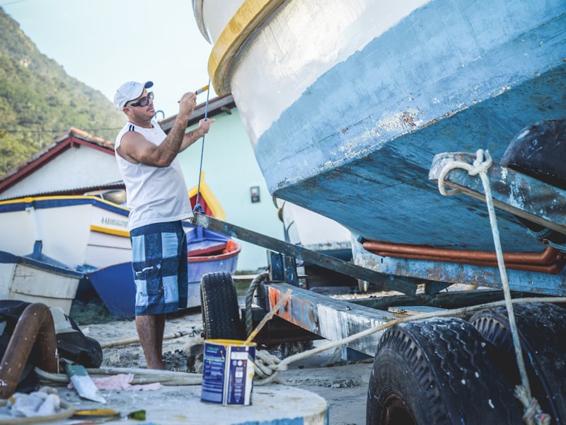 A man working on the freshly painted hull of a boat in bright sunshine