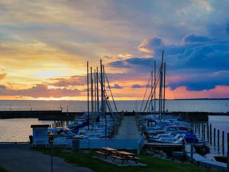 Boats moored along a jetty as the sun sets behind a dramatic sky