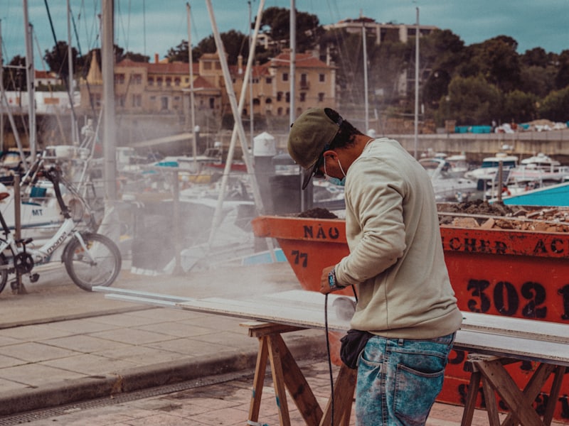 A technician sanding a boat panel on trestles beside a marina