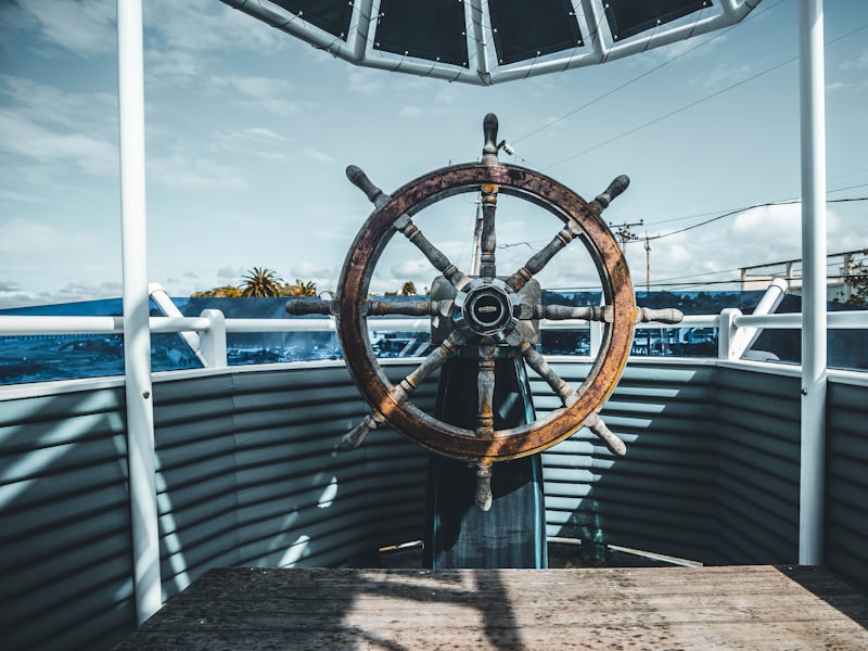 A traditional wooden ship's wheel on an open deck under blue sky