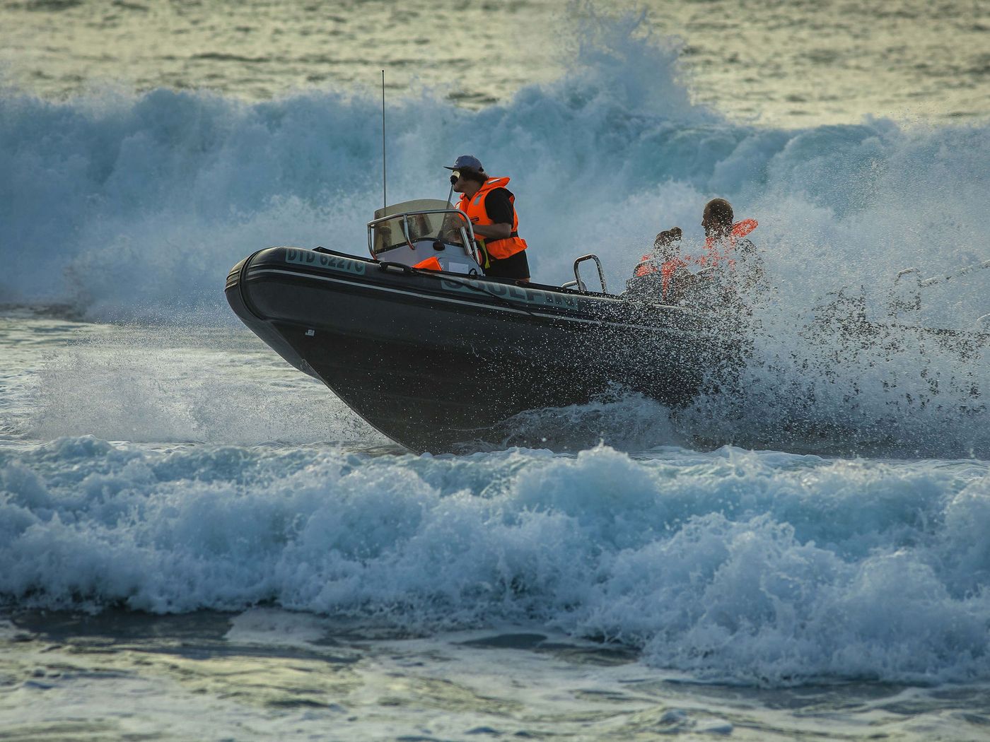 A rigid inflatable boat launching through breaking surf with the skipper standing at the helm