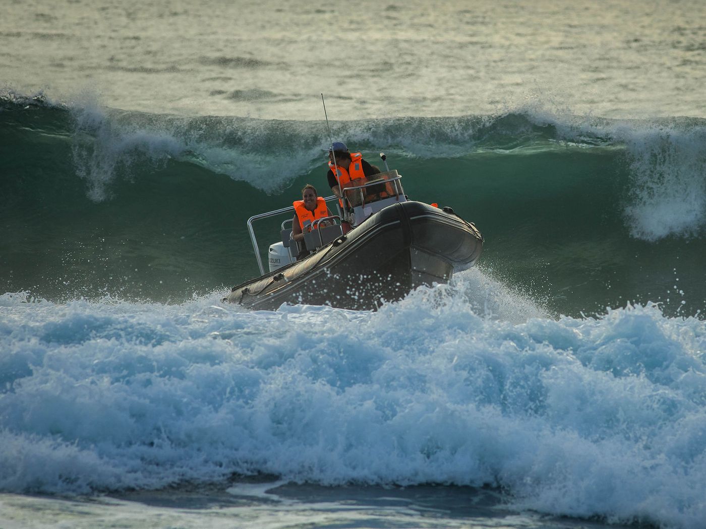 A skipper and passenger in life jackets taking a rigid inflatable boat over a breaking wave