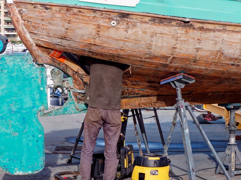 A technician working underneath a wooden hull supported on stands