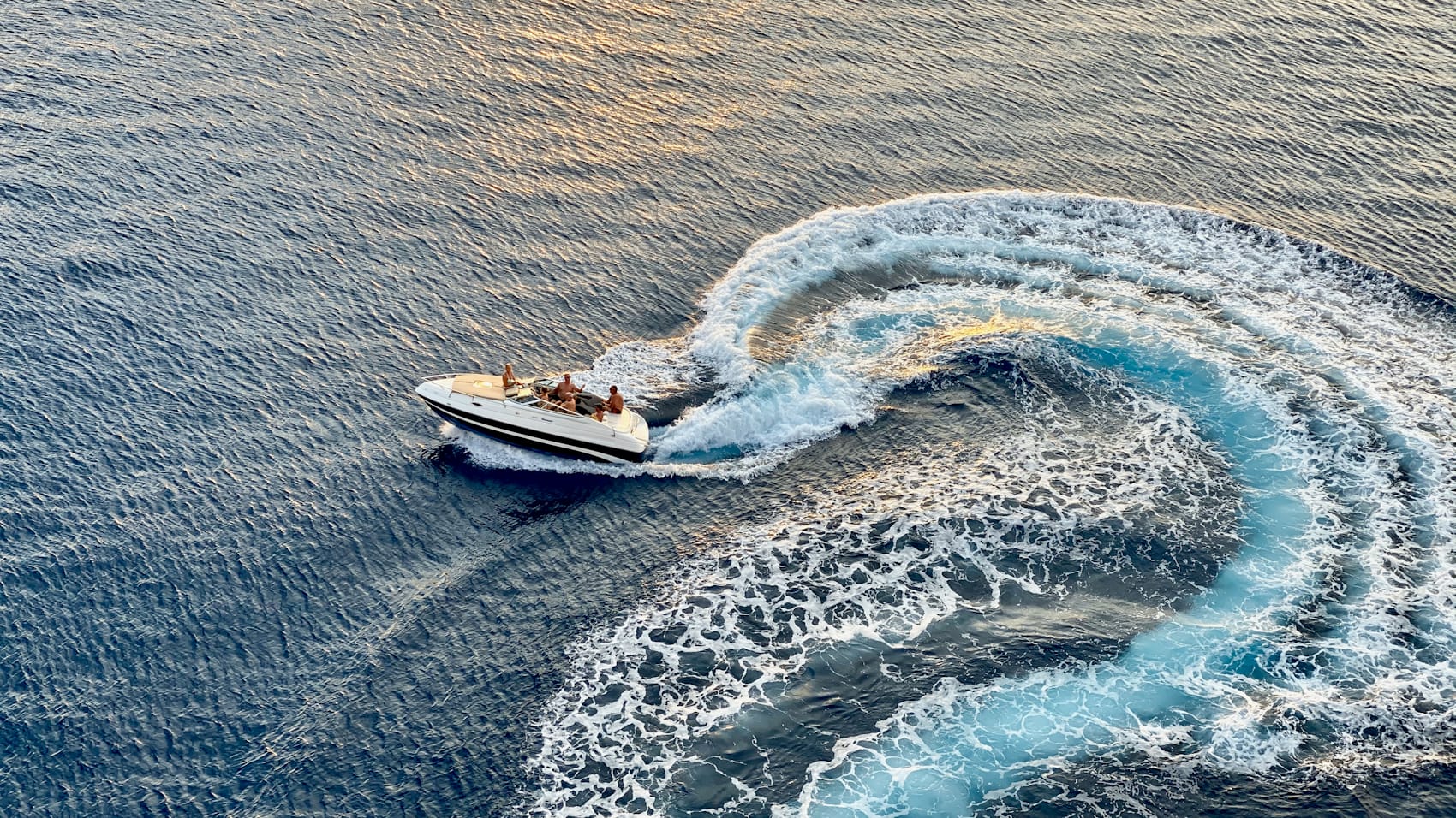 A powerboat carving a turn across the open ocean at golden hour