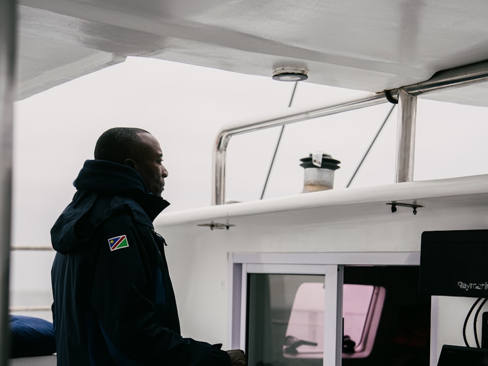 A skipper at the helm of a boat, hands on the wheel