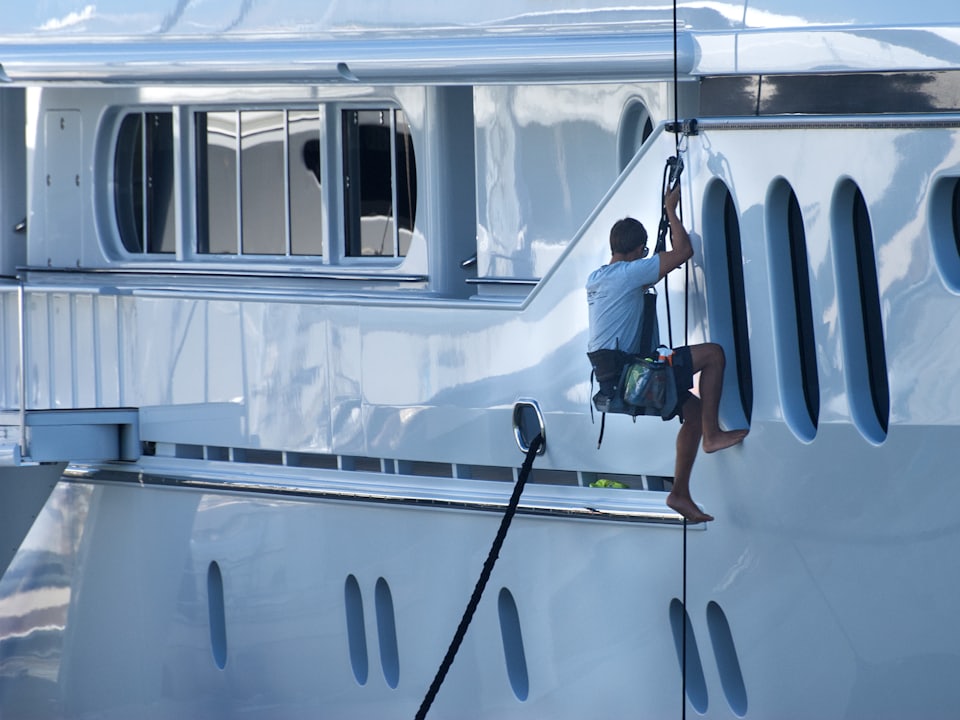 A crew member cleaning the gleaming white hull of a large motor yacht